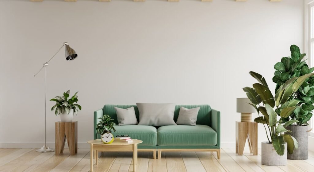 Este salón minimalista y luminoso combina el estilo escandinavo con toques naturales, destacando un sofá verde suave que armoniza perfectamente con la madera clara del suelo y los muebles. La presencia de plantas grandes para interiores, como las colocadas en la esquina derecha, no solo aporta frescura y color, sino que también equilibra el espacio visualmente, creando un ambiente sereno y acogedor ideal para el descanso o la lectura.